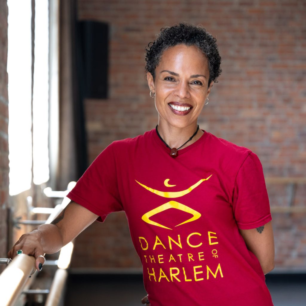 Tai Jiminez, the Director of the Dance Theatre of Harlem School is wearing a red shirt with the school logo and smiling at the camera.