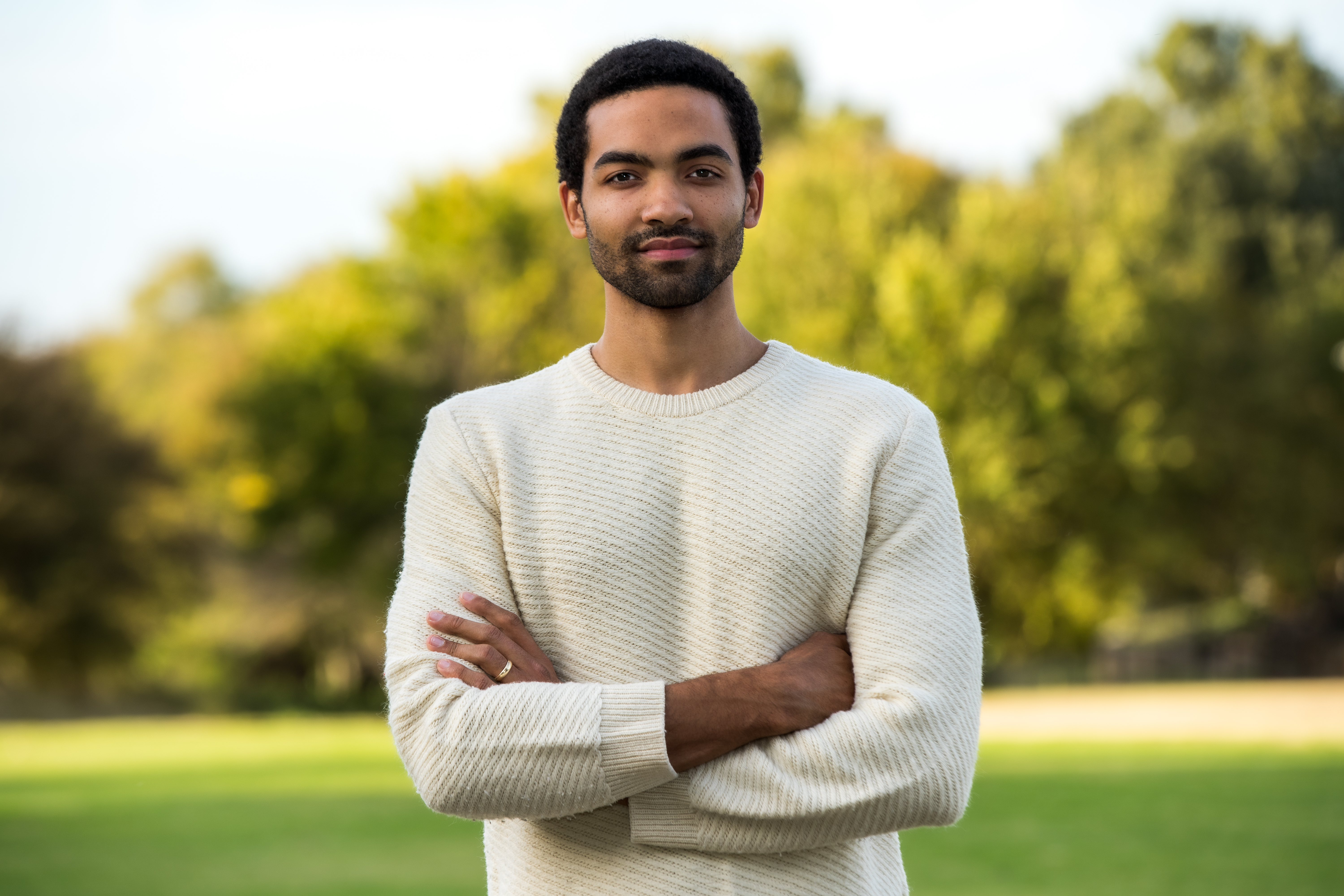 Silas Farley with folded arms, stands outside and smiles at camera
